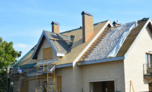 Roofing contractors installing asphalt shingles on a light-colored residential property.
